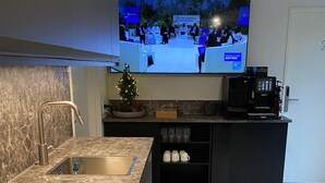 Una cocina moderna con encimera de mármol, pileta integrada, cafetera y televisor mostrando un noticiero.