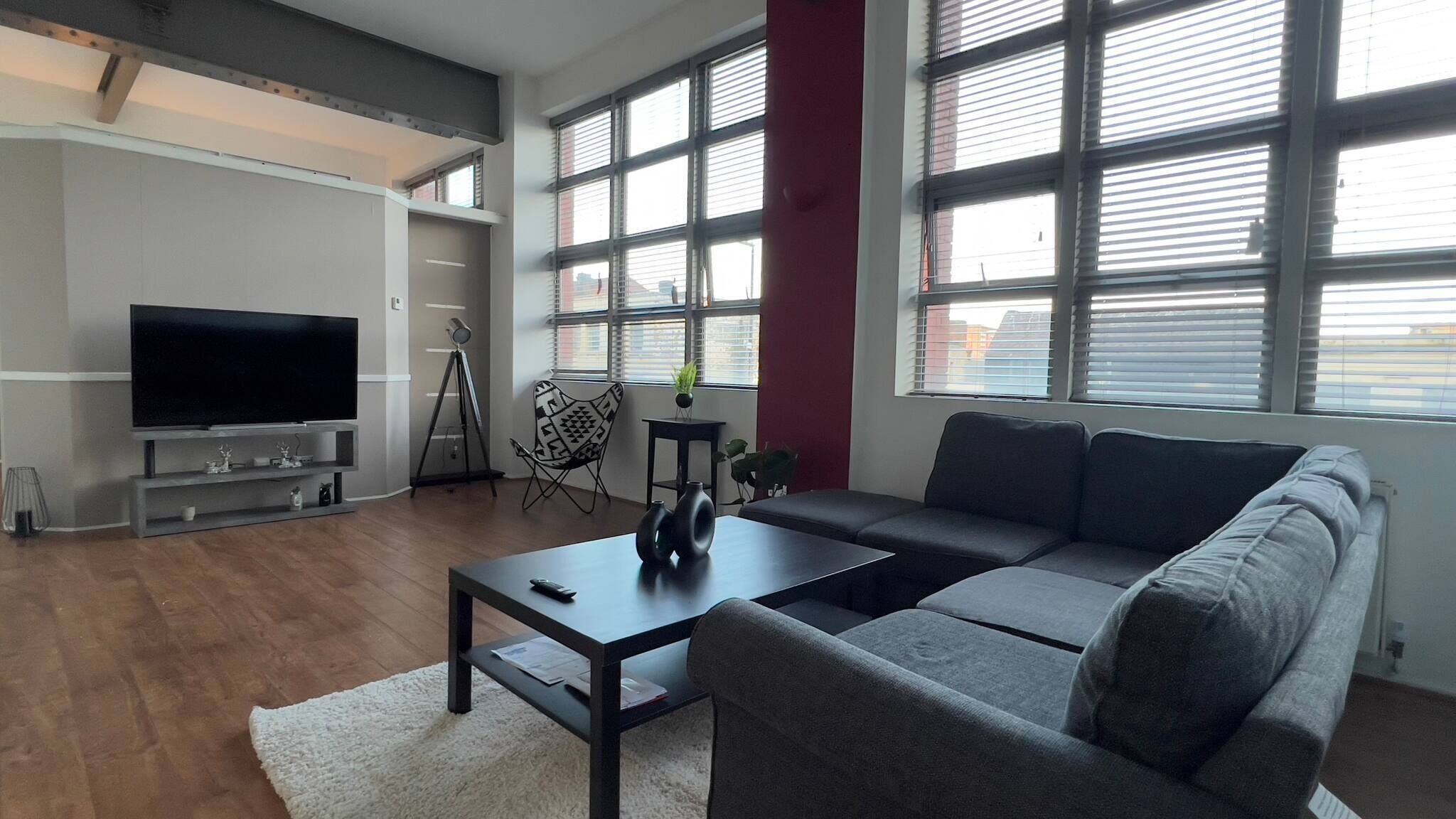 A modern living room with a large flat-screen TV, a sofa, a coffee table, and a tripod lamp.