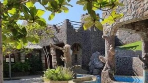 Ein Innenhof mit Steinmauern, einer Fontäne und viel Grün.