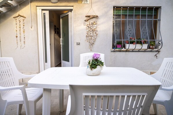 Una mesa blanca con sillas, una planta decorativa y una ventana con plantas.