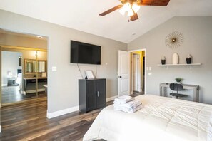 Ein Schlafzimmer mit einem großen Bett, einem Flachbildfernseher, einem Deckenventilator, einem Kleiderschrank und einem Spiegel.