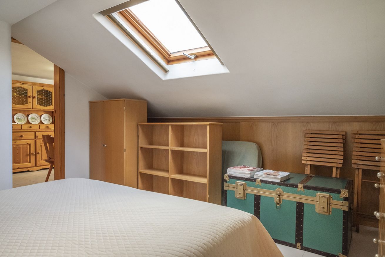 A bedroom with a skylight, a bed, a wooden wardrobe, and a green suitcase.