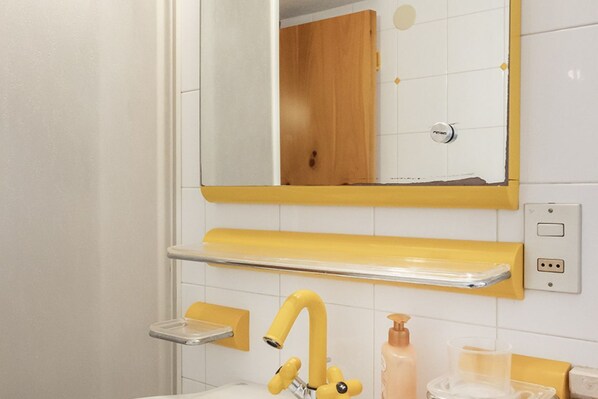 A bathroom with a yellow sink, a mirror, and a soap dispenser.