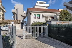 A residential building with a gated entrance, a gravel driveway, and a metal fence.