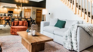 A spacious living area with a high ceiling, a wooden staircase, a dining area, and a cozy seating arrangement. - FallWater - 5BR Lakehouse, WtrFrnt, Ht Tub, F/pit. Close to Ski and Golf! (Boyne City)
