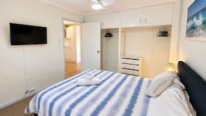A bedroom with a bed, a TV, a wardrobe, and a painting.
