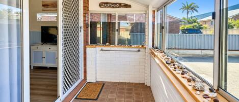 A hallway with a white tiled floor, a wooden bench with seashells, and a sign that reads 'DRIFTWOOD'.