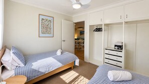 A bedroom with two beds, a wardrobe, and a ceiling fan.