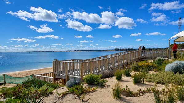 A wooden boardwalk leading to a beach with a clear view of the water and a distant shoreline.