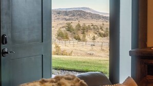Una habitación con un ventanal grande, una puerta y vistas a un paisaje con colinas y una cerca.