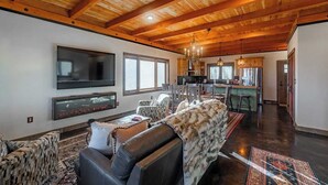 Un salón espacioso con chimenea, un televisor grande y un comedor con una cocina al fondo.