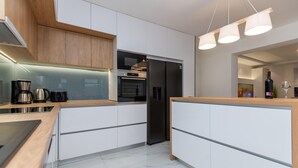 Une cuisine moderne avec des meubles blancs, un réfrigérateur noir, une machine à café et une bouteille de vin.