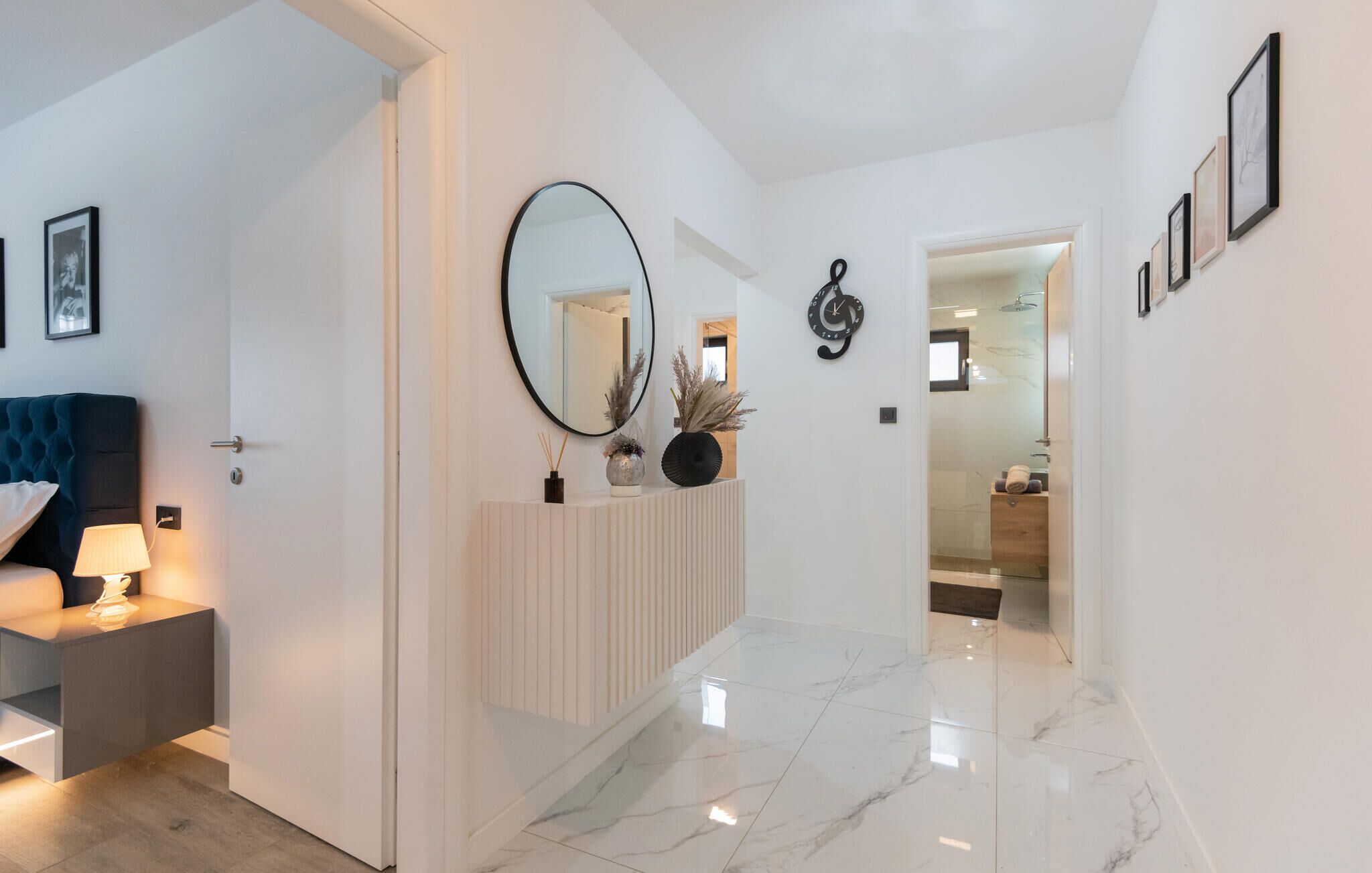 A modern hallway with a white door, a round mirror, and a clock on the wall.