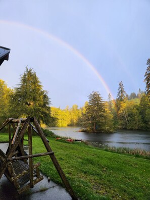 Un columpio de madera cerca de un lago, con un arcoíris al fondo.