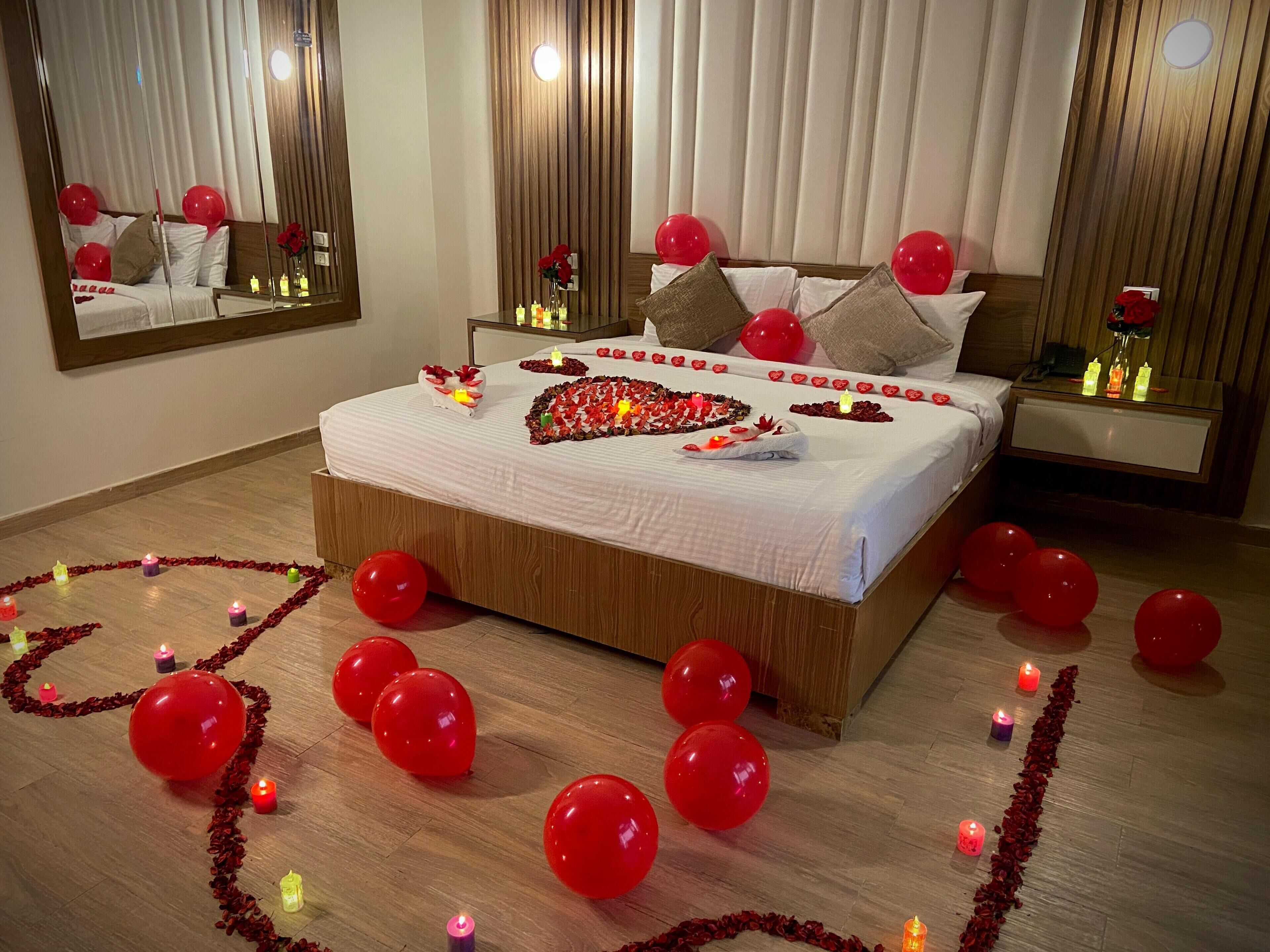 A bedroom with a large bed, red balloons, candles, and a heart-shaped decoration on the bed.
