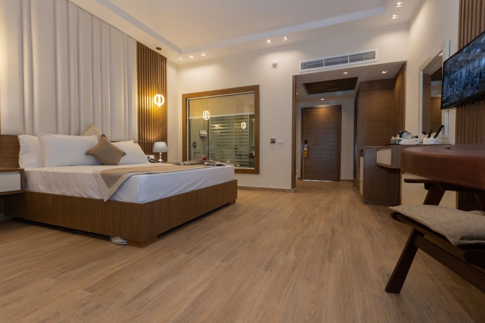 A modern hotel room with a large bed, a desk, and a bathroom visible through a glass door.