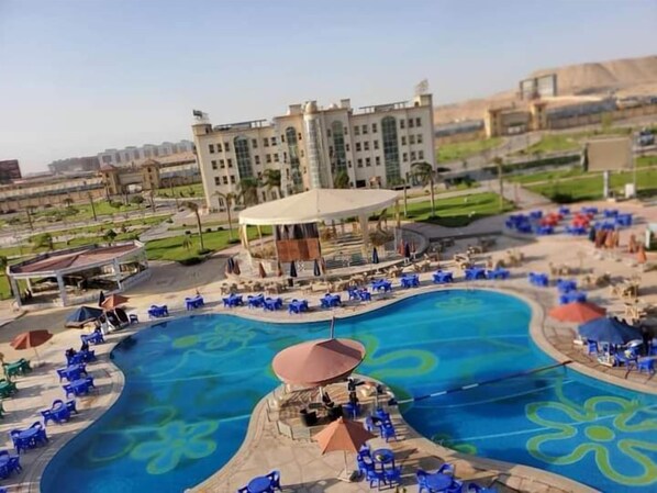 A swimming pool with blue chairs and umbrellas, surrounded by a building with a dome structure. - Ramage Hotel & Resort (Cairo)