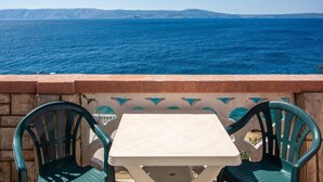 Una mesa y dos sillas en un balcón con vista a una masa de agua y formaciones terrestres distantes.