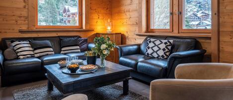 A cozy log cabin interior with two leather sofas, a coffee table, and a vase with flowers.