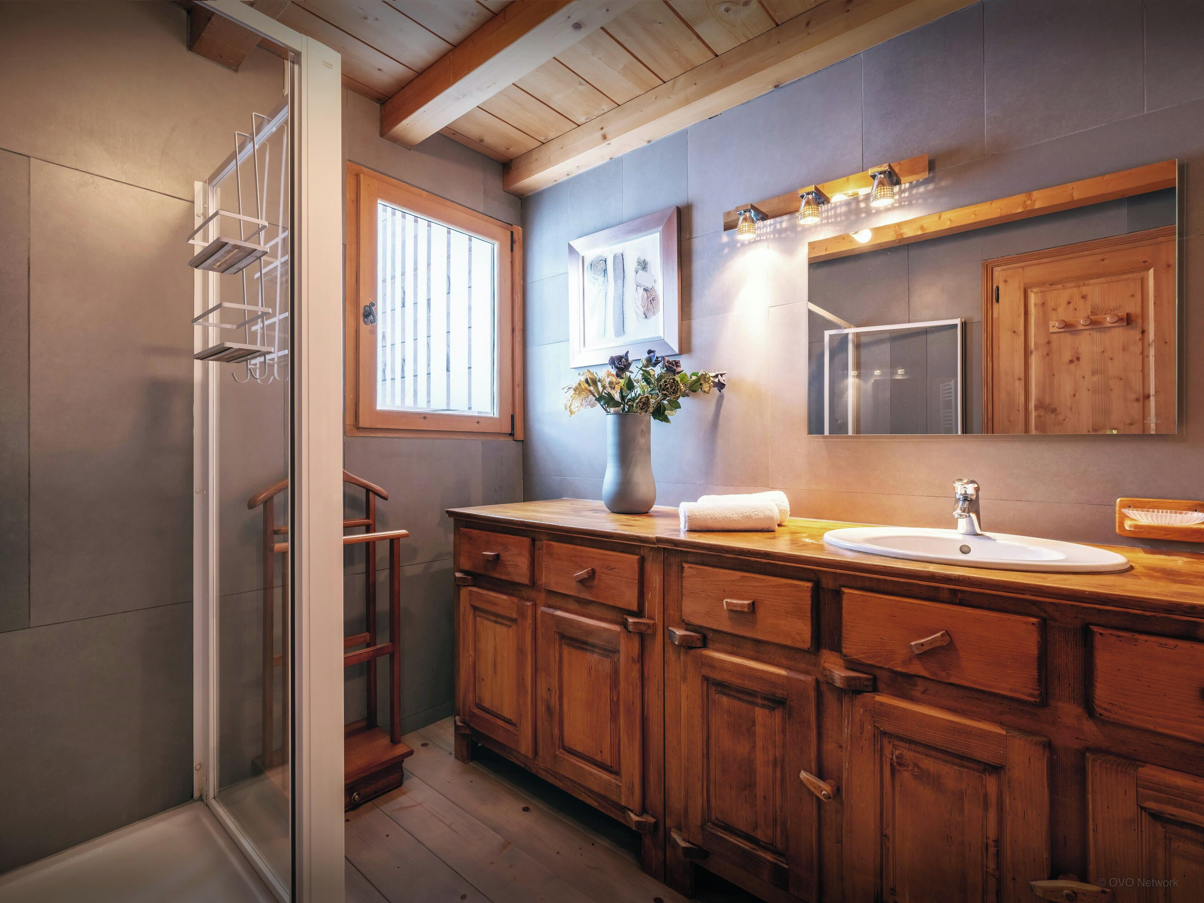 Ein Badezimmer aus Holz mit einem großen Spiegel, einem Waschbecken und einer Holzkommode.