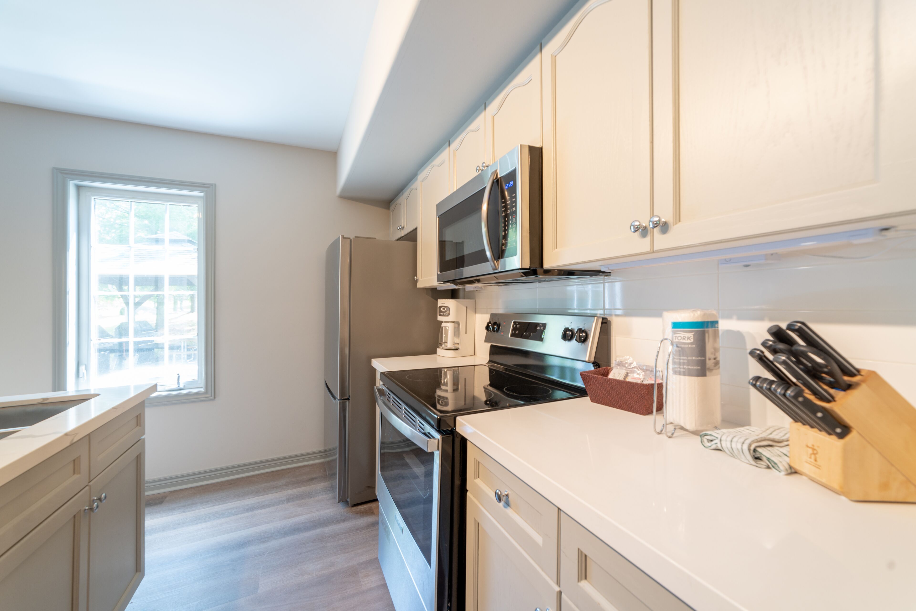 A modern kitchen with stainless steel appliances, white cabinetry, and a window providing natural light.