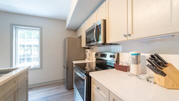 A modern kitchen with stainless steel appliances, white cabinetry, and a window providing natural light.