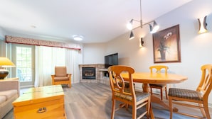 Een woonkamer met een open haard, een eettafel met stoelen, een bank en een houten dressoir.