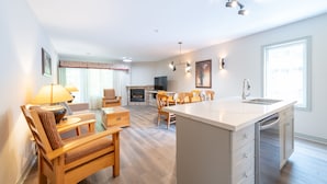 Een ruime woonkamer met een open haard, houten meubels, een keukeneiland en een groot raam dat zorgt voor natuurlijk licht.
