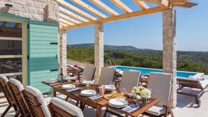 An outdoor dining area with a pool view, wooden pergola, and stone pillars. - Gorgeous home in Primosten (Primosten)