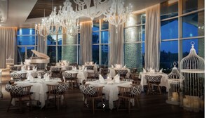 A dining area with multiple tables set for a meal, large windows, and decorative chandeliers. - Cozy retreat, has something for everyone,property has golf course and lazy river (Las Jarretaderas)