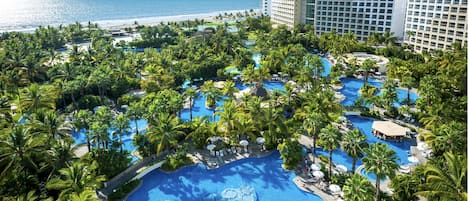 A resort with multiple swimming pools surrounded by palm trees, a beach, and ocean views.