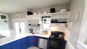 Een keuken met blauwe kastjes, een zwart fornuis en witte aanrechtbladen.
