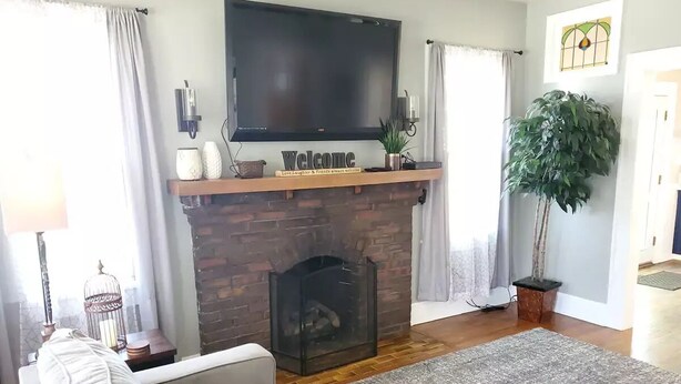 Een woonkamer met een open haard, een televisie erboven en een bank.