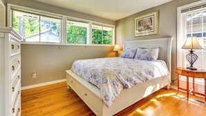 Un dormitorio con cama, cómoda, ventanas y lámpara.