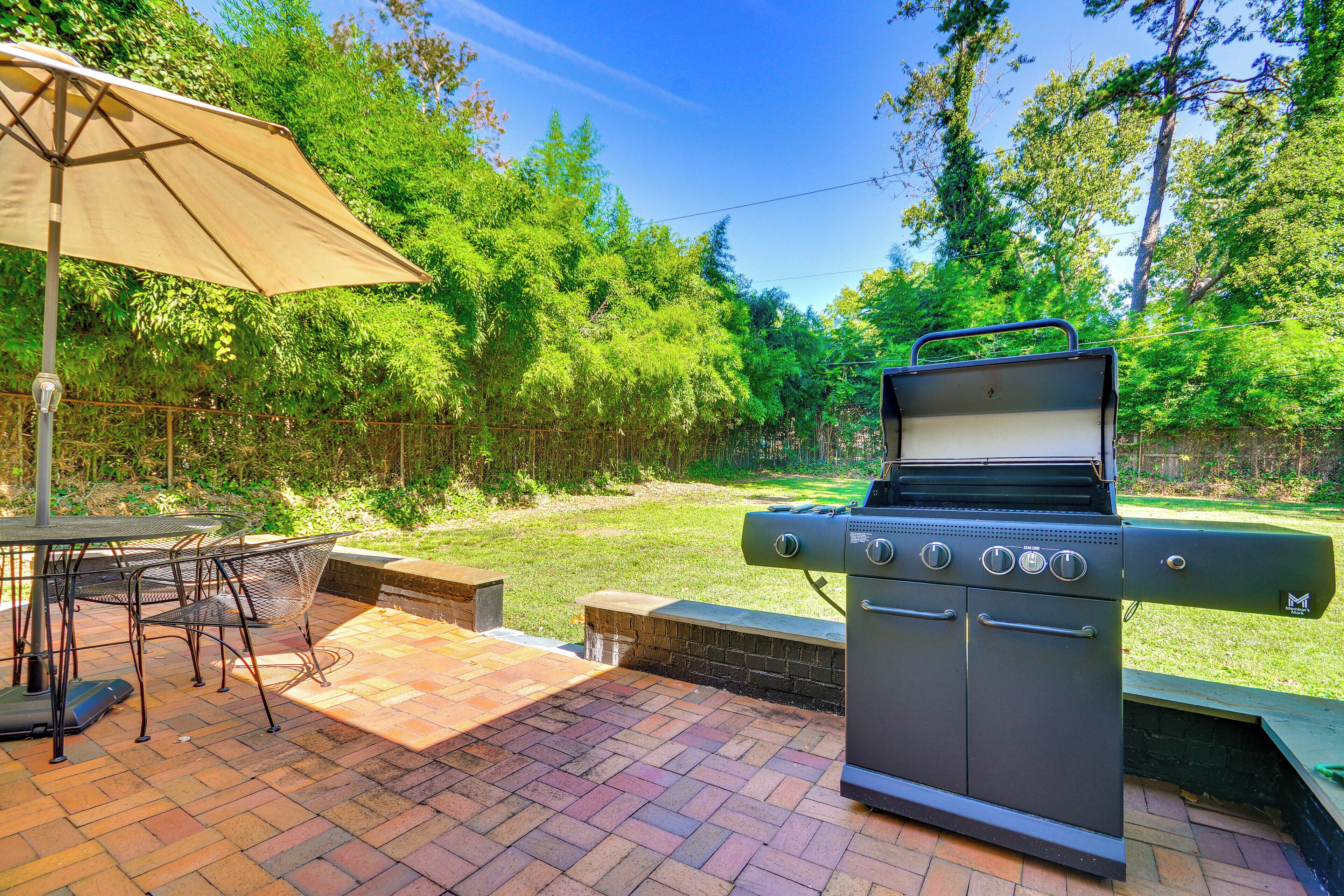 An outdoor patio with a grill, chairs, and an umbrella.
