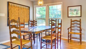 Comedor con una gran mesa de vidrio rodeada de sillas de madera, ventanas amplias y una lámpara colgante.