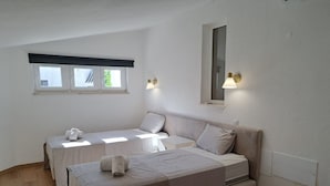 Un dormitorio con dos camas individuales, un sofá grande, una mesita y una ventana con persianas.