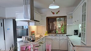 Cocina compacta con armarios blancos, estufa integrada, lavamanos y ventana con persianas.