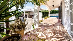 Un espacio al aire libre cubierto con un sendero adoquinado, piscina y un edificio blanco con arcos.