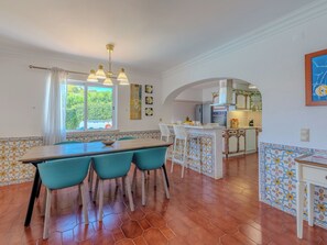 A dining area with a wooden table and teal chairs, a kitchen with a tiled backsplash, and a view through a window. - Libertos V4 - VIP Properties by Interhome (Albufeira)