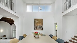 A spacious dining area with a high ceiling, a large painting, and a view of the outdoors.