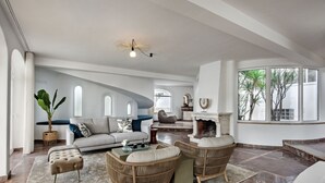 A spacious living room with a fireplace, comfortable seating, and large windows offering a view of the outdoors.