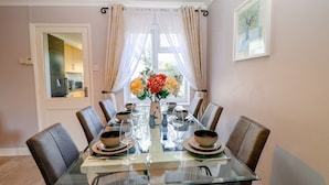 Un coin repas avec une table en verre, des chaises marron et un vase de fleurs.