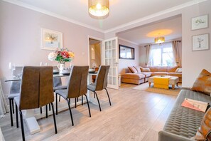 A modern living room with a dining area, featuring a sofa, a coffee table, and a dining table with chairs. - Country View Cottage - sleeps 5 guests  in 3 bedrooms (Beighton)