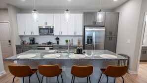 A modern kitchen with white cabinets, stainless steel appliances, and a central island with bar stools. - Modern, New Apt | Pool | Long Stays (Athens)