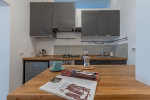 A kitchen with dark cabinets, a wooden countertop, a coffee maker, and a magazine.
