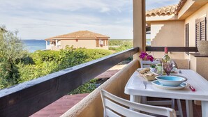 A balcony with a table set for dining, overlooking a coastal view with a building in the distance. - F4 - F2, Baia de Bahas by Interhome (Golfo di Marinella)