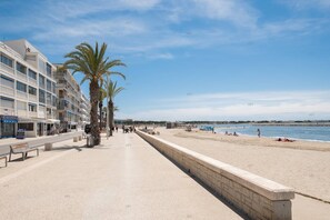 Een kustpromenade met een rij palmbomen, een strand en een rij gebouwen met balkons.
