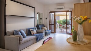 Una sala de estar moderna con un sofá, una mesa de comedor y una cocina visible a través de una puerta abierta.