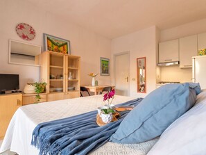 Une chambre avec un lit, une télévision, une armoire en bois et un coin cuisine.